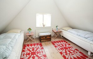 Un dormitorio ático pequeño y triangular con dos camas individuales, un radiador, una ventana con vistas y un cofre de madera.
