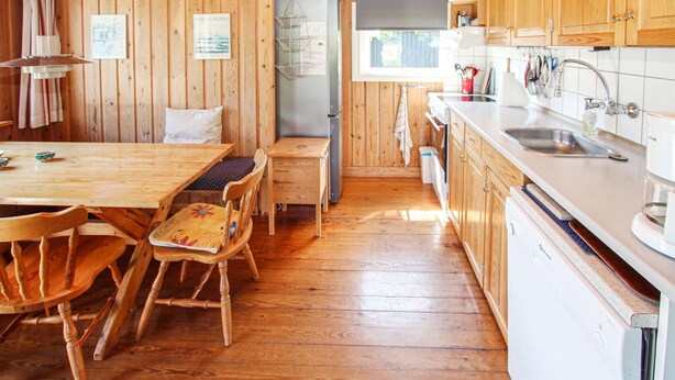 Ein Holzinterieur mit einem Esstisch, Stühlen, einer Küchenzeile mit Spüle und Schränken sowie einem Fenster.
