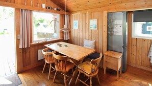Eine Holzhütte mit Esstisch, vier Stühlen, einem kleinen Hocker und einem Kühlschrank.
