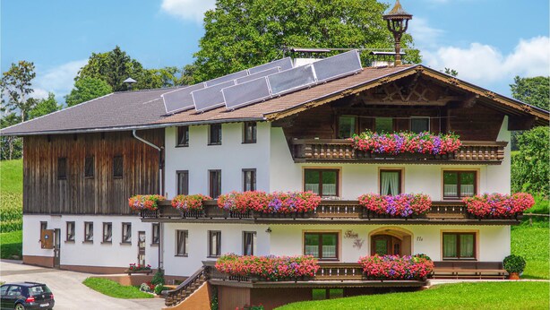 Un chalet à deux étages, doté d’un toit en pente, de panneaux solaires et de jardinières sur le balcon.