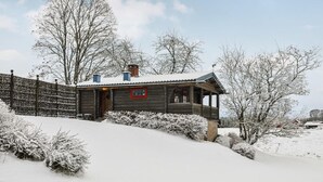 Una cabaña de madera con porche, rodeada de árboles cubiertos de nieve y una valla de madera.