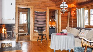 Interior acogedor de una cabaña de madera con chimenea, un sofá, una mesa de comedor y un tapiz colgante.