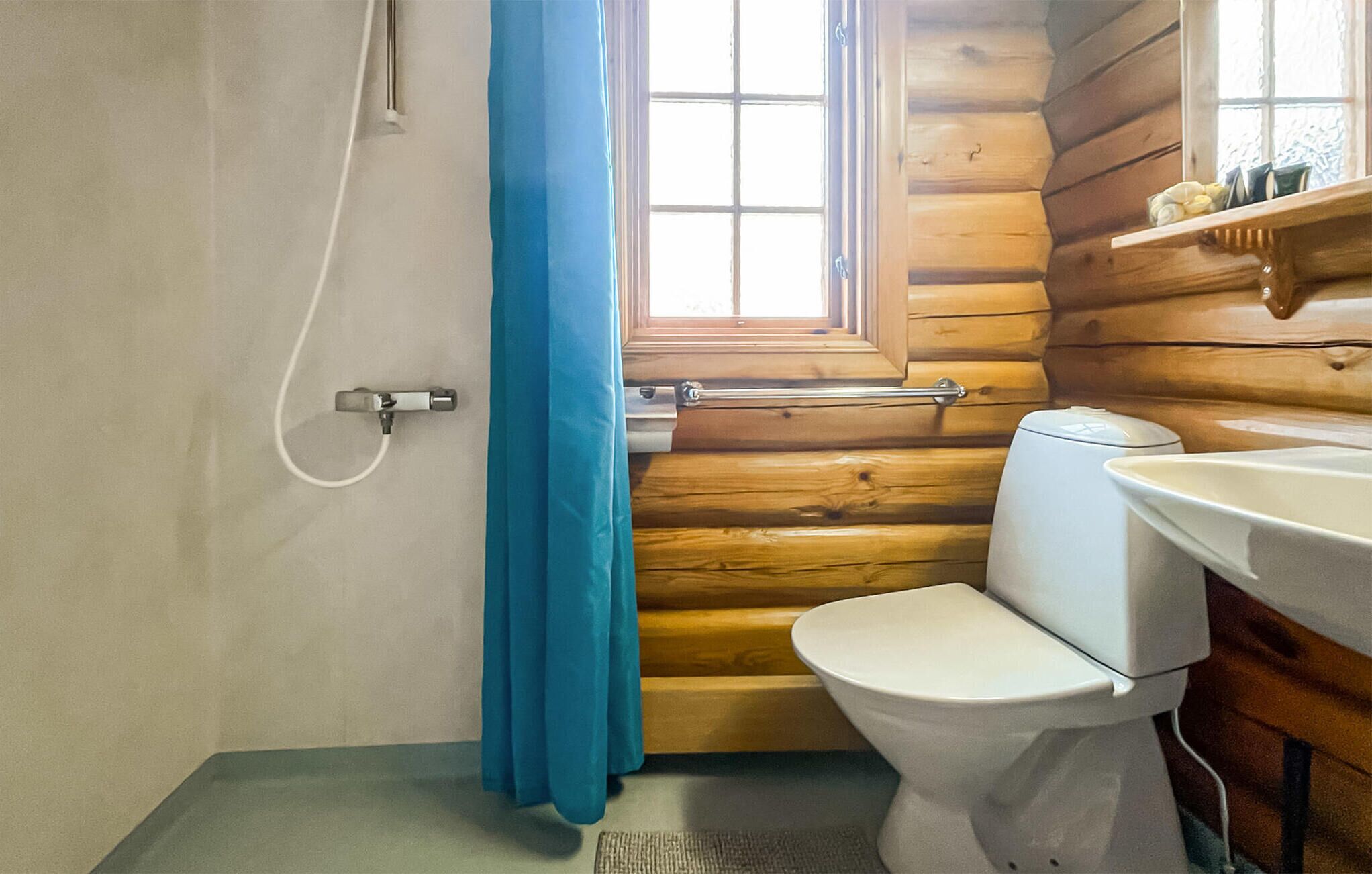 A small, compact bathroom with a wooden interior, a white toilet, a sink, and a window with a view of the outdoors.