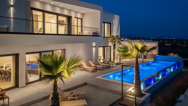 Uma casa moderna de dois andares com piscina no terraço, área de estar externa e palmeiras.