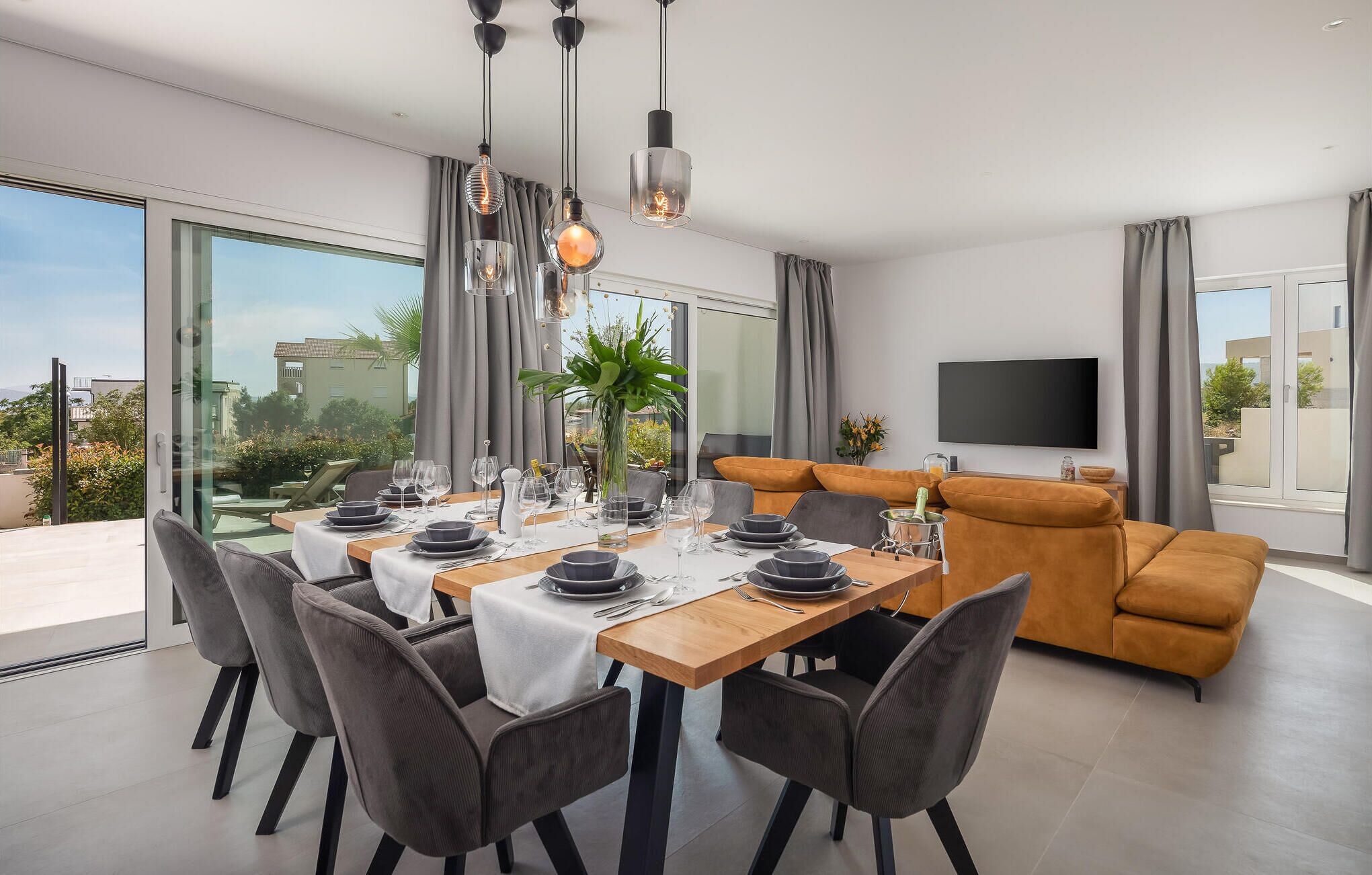 A modern dining area with a wooden table set for four, surrounded by grey upholstered chairs.