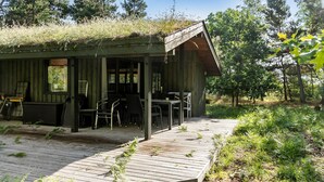 Una cabana rústica amb terrassa de fusta, zona d'estar coberta a l'exterior i entorn natural.