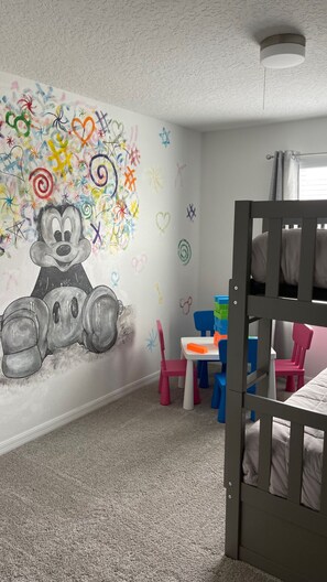 A child's room with a colorful wall mural, a bunk bed, and a small table with toys.