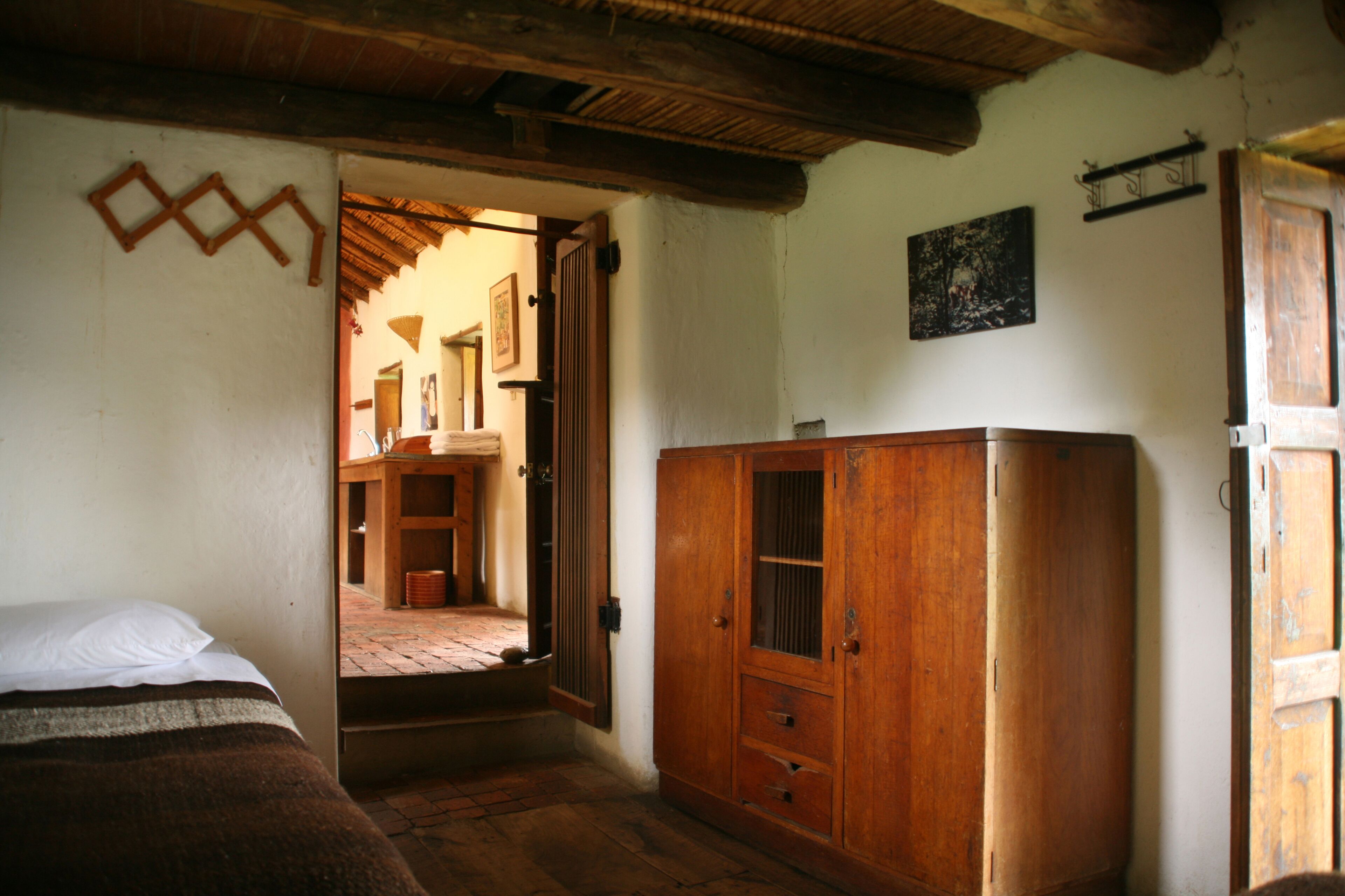 Een kamer met een houten garderobe, een bed met een gestreept dekbed en een deur die naar een andere kamer leidt.