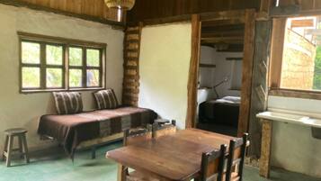 A rustic room with a wooden table and chairs, a bench with pillows, a window, and a door leading to another room.