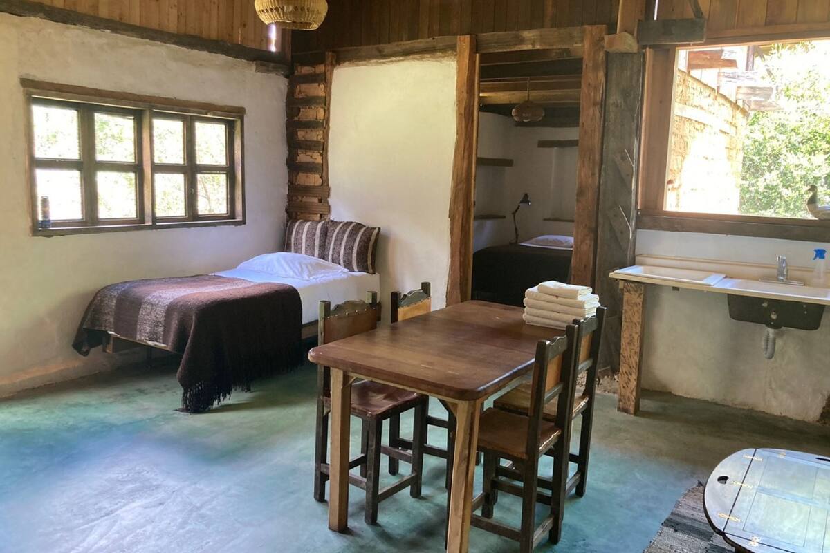 Een eenvoudige kamer met een bed, een houten tafel, een wastafel en een raam.