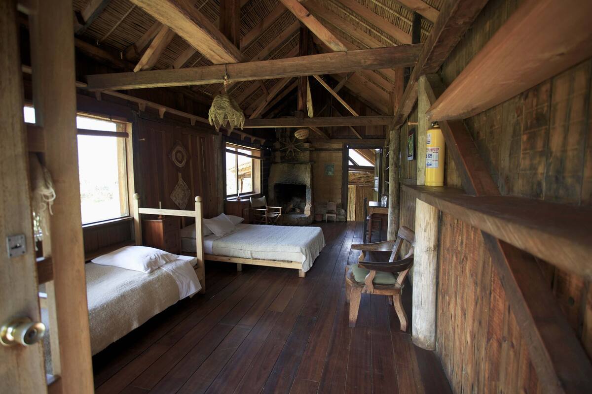 Een rustiek blokhut interieur met een houten bed, een open haard en een houten eettafel.