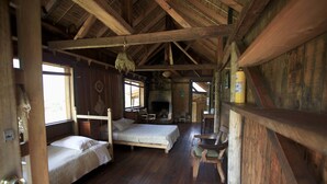 Interior rústico de una cabaña con dos camas de madera, una chimenea de piedra y una mesa de comedor de madera.