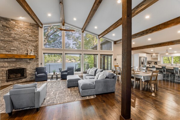 A spacious living area with a stone fireplace, large windows, and a dining area with wooden flooring.