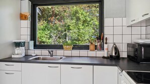 Una cuina moderna amb vistes a la verdura per la finestra, una cafetera i un búl de tè a la superfície.