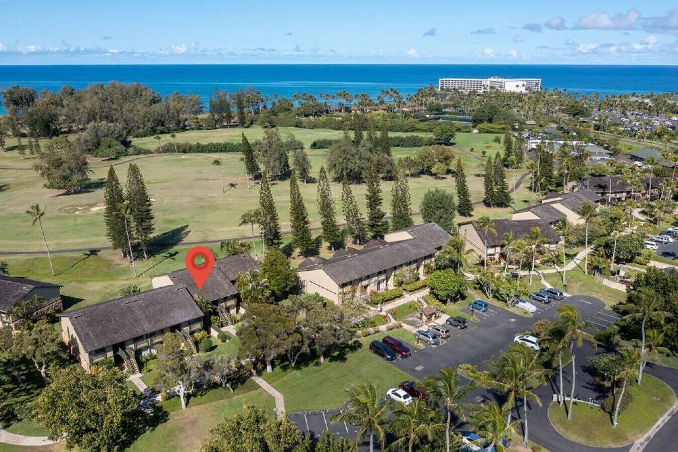 An aerial view of a resort with multiple buildings, a parking area, and a large body of water in the background.