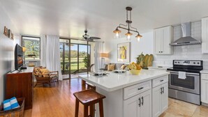 A modern kitchen with white cabinets, a large island, and a dining area with a view of the outdoors. - Spacious 1 Bedroom Condo at Turtle Bay (Kahuku)