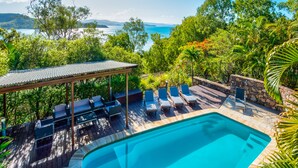 Ein Poolbereich mit Liegestühlen und einer überdachten Sitzgelegenheit, umgeben von üppiger Vegetation und Blick auf das Meer.