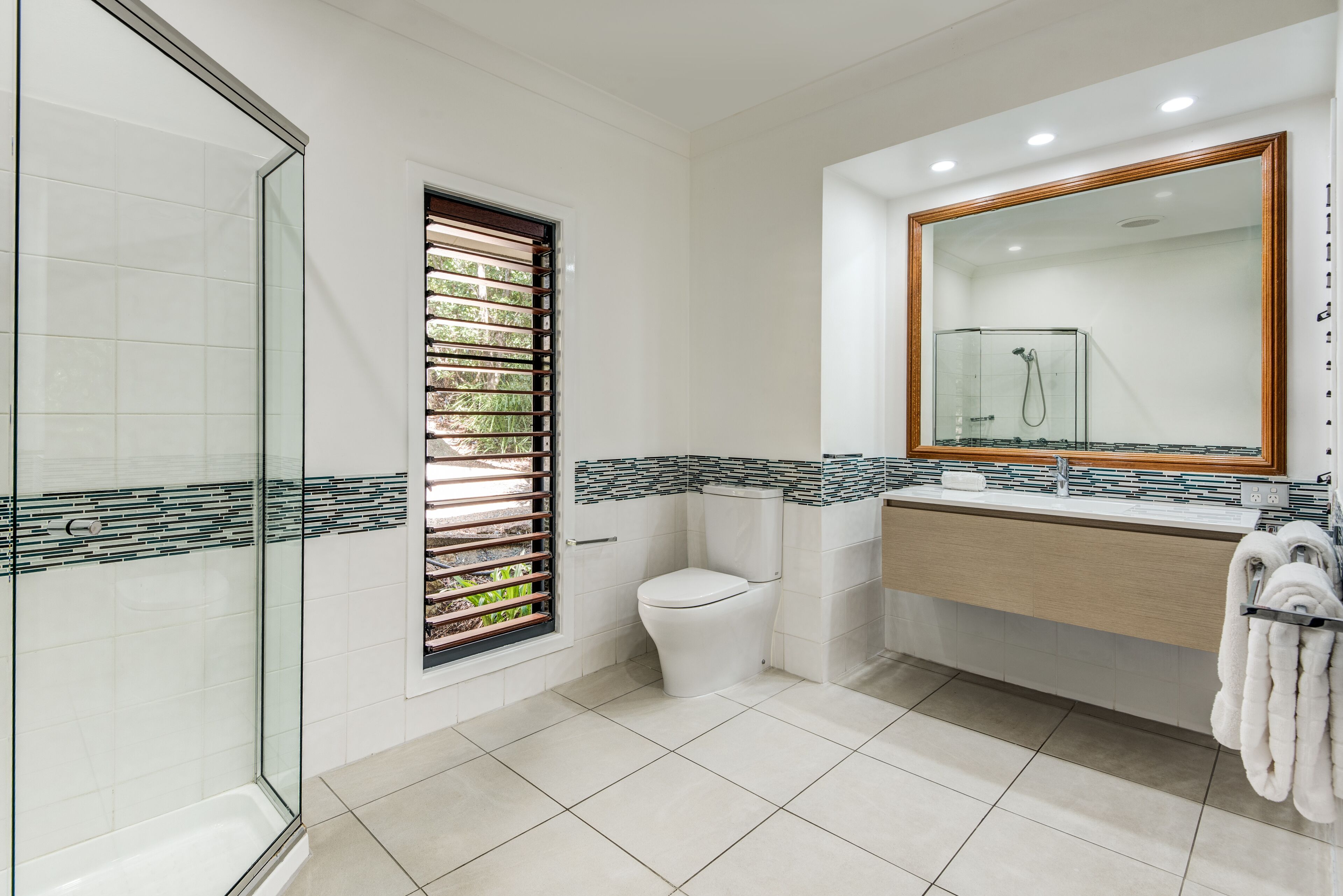 A modern bathroom with a glass shower enclosure, a toilet, and a sink with a mirror above it.