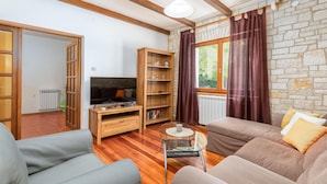 A cozy living room with a stone wall, wooden beams, a TV, a bookshelf, and a sofa. - Pet friendly home in Svetvincenat (Svetvincenat)
