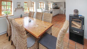 Un'area pranzo con un tavolo di legno e sedie in vimini, una cucina sullo sfondo e una stufa a legna nera.