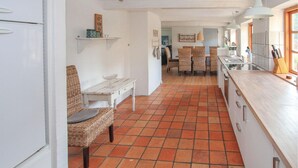 Una cucina con pavimento piastrellato, mobili bianchi, un'area pranzo con sedie in vimini e un tavolo bianco.