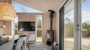 A modern interior with a wooden wall, a black stove, a TV, and a dining area with a striped rug. - 5 bedroom amazing home in Glesborg (Glesborg)