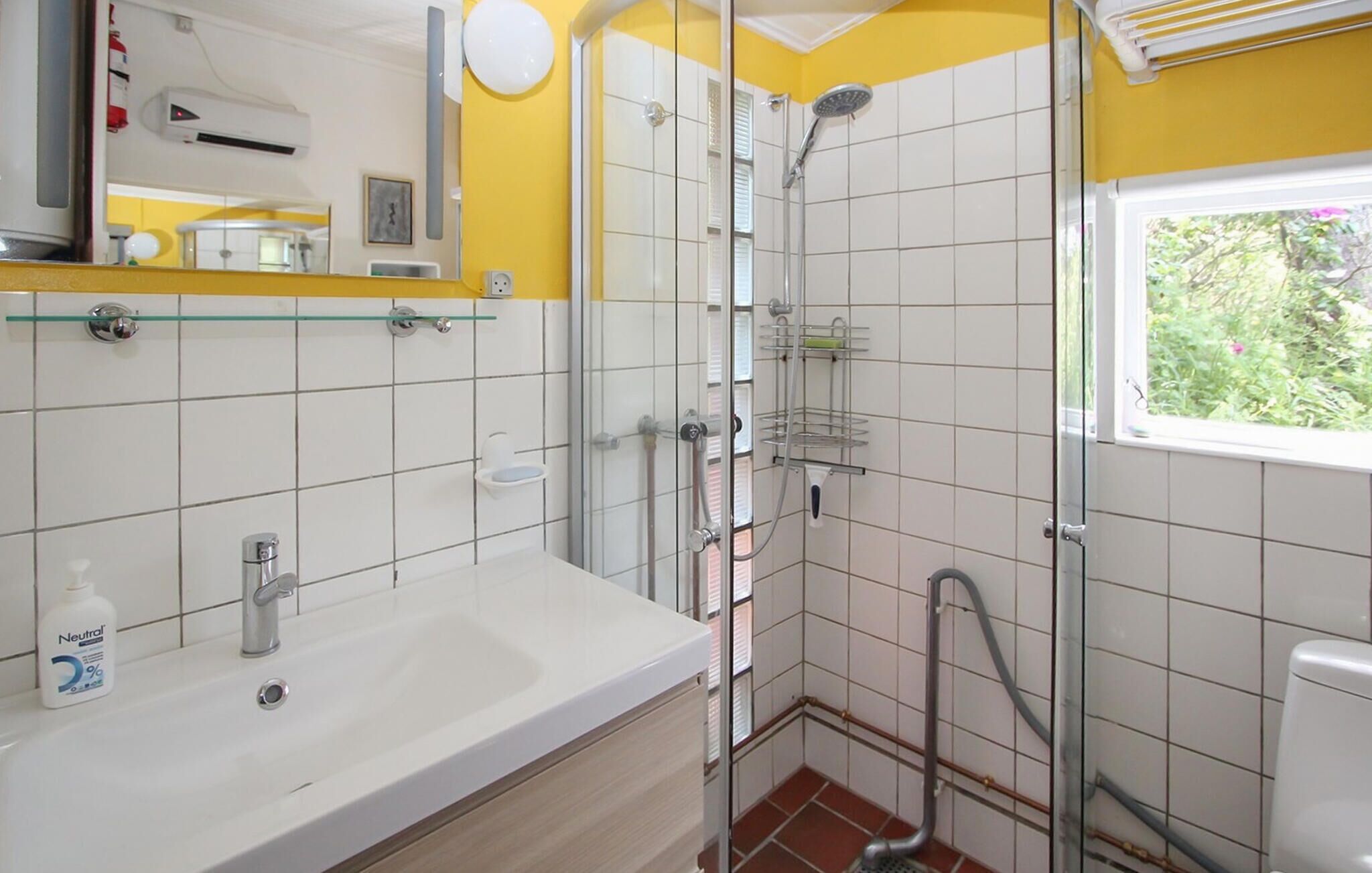 A bathroom with a white sink, a glass shelf, a shower, and a window.