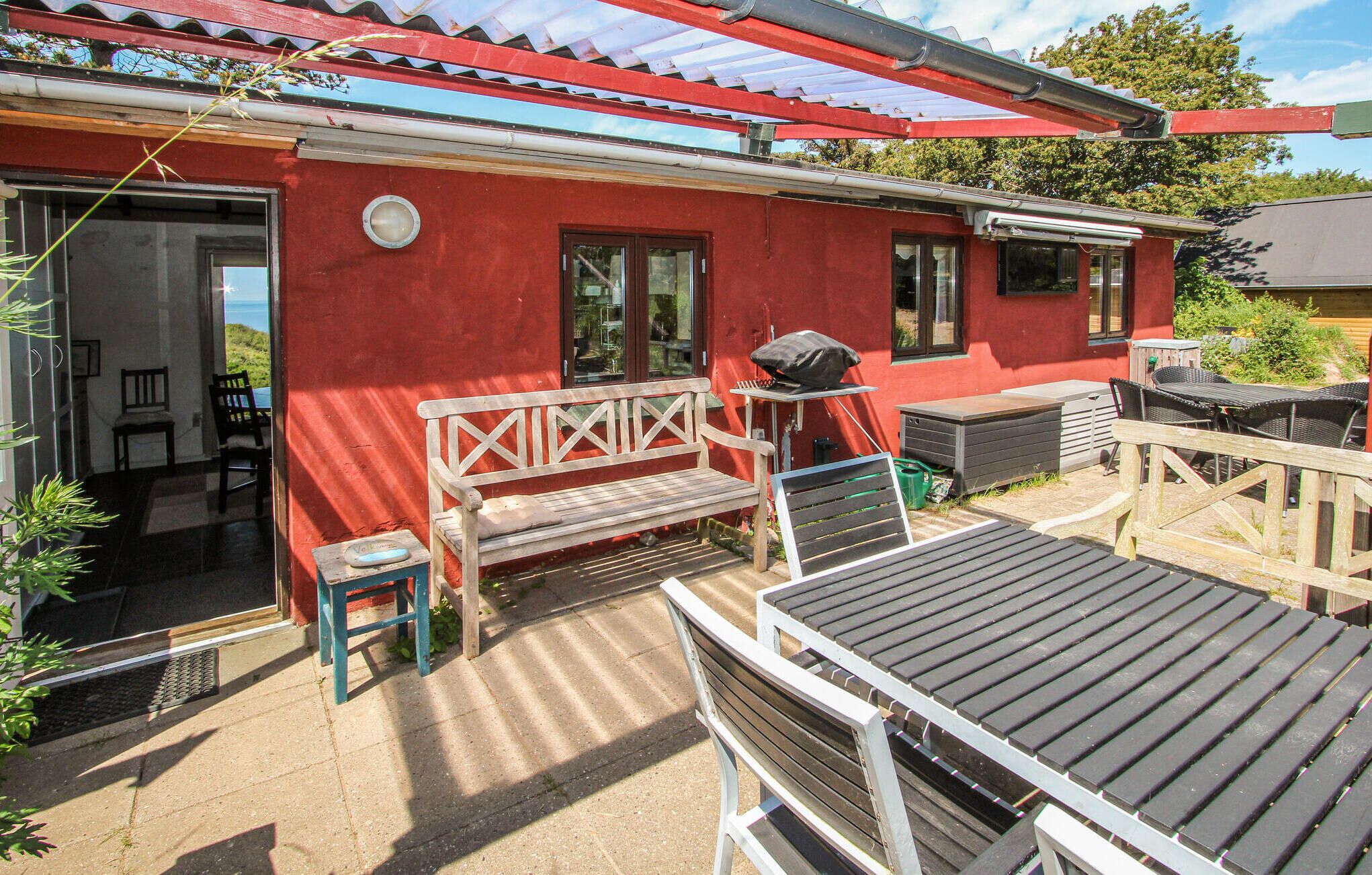 Ein rotes Gebäude mit einer überdachten Terrasse, Holzbanken und Außenbestuhlung.