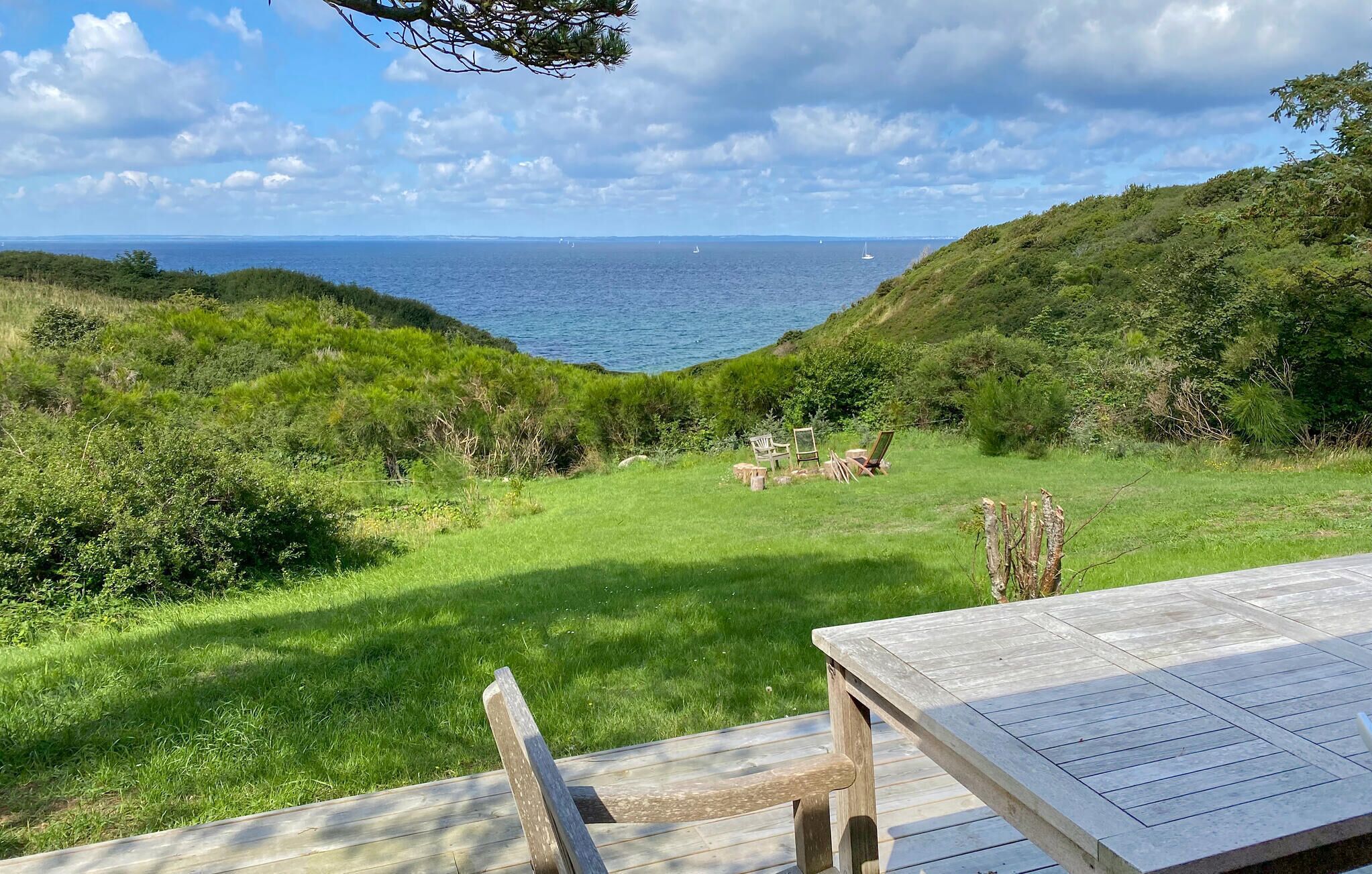 Um deck de madeira com vista para uma área gramada e o mar, com terra distante ao fundo.