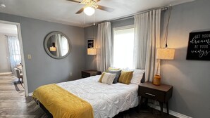 A bedroom with a bed, a ceiling fan, a round mirror, a bedside table with a lamp, and a motivational quote on the wall. - Janie’s cozy cottage minutes from Texas A&M Kingsville (Kingsville)