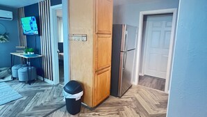 A room with a herringbone wooden floor, a wooden cabinet, a refrigerator, and a television mounted on the wall. - Janie’s cozy cottage minutes from Texas A&M Kingsville (Kingsville)