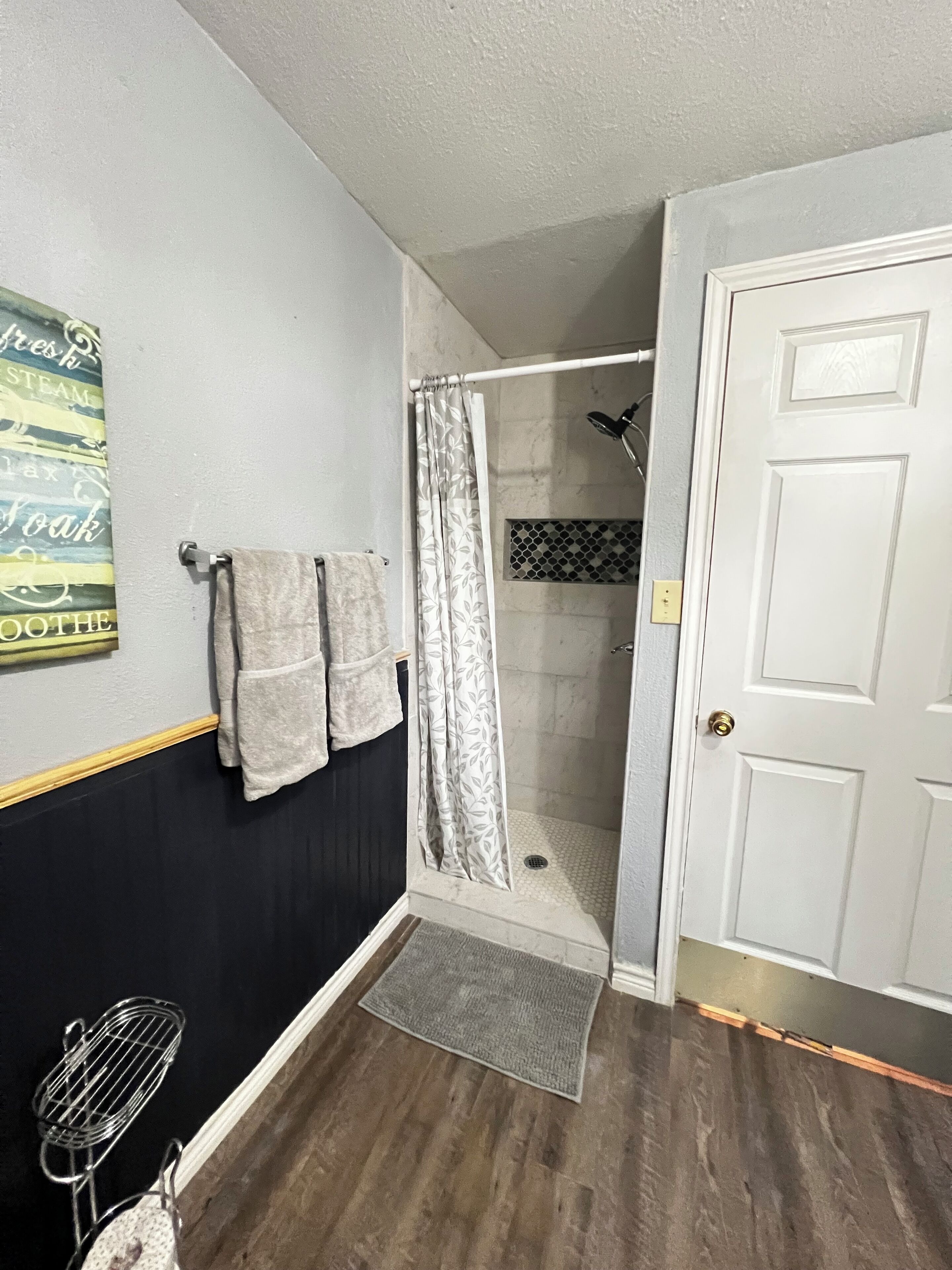 A bathroom with a shower, a towel rack with towels, a shower curtain, and a door.