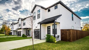 A modern two-story residential building with a covered front porch, a wooden fence, and a well-maintained lawn. - Spacious 4BR Retreat, Sleeps 10, Backyard + Near Dallas (Dallas)