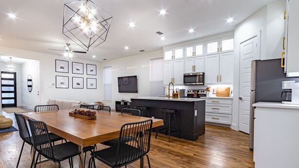 A modern kitchen with white cabinets, a wooden dining table, and black chairs. - Spacious 4BR Retreat, Sleeps 10, Backyard + Near Dallas (Dallas)
