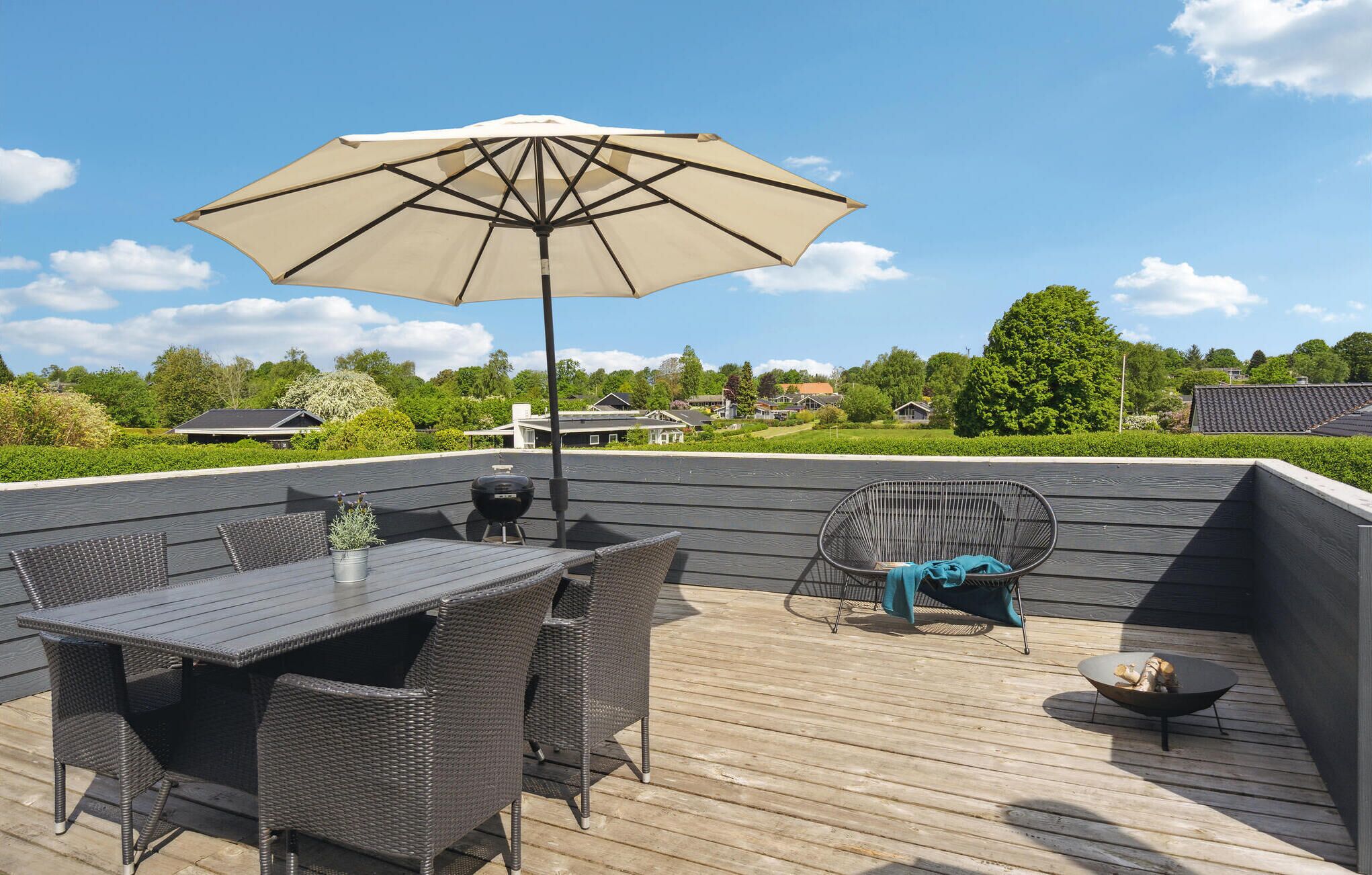 Une terrasse extérieure avec une table et des chaises, un barbecue et un grand parasol.