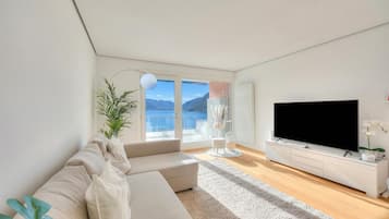 Ein modernes Wohnzimmer mit einer Couch, einem Flachbildfernseher, einer Pflanze und Blick ins Freie.