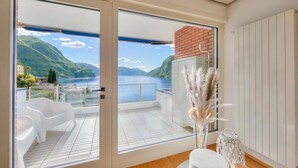 A balcony with a view of mountains and a lake, white chairs, and a white table with a vase of pampas grass. - Honeymoon With Panoramic Lake-view (Lugano)