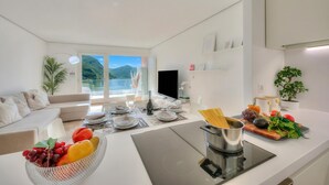 A modern kitchen with a dining area, a flat-screen TV, and a view of mountains. - Honeymoon With Panoramic Lake-view (Lugano)