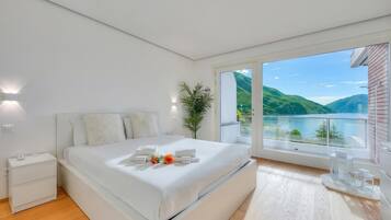 A modern bedroom with a large bed, a nightstand, a potted plant, and a view of a lake.