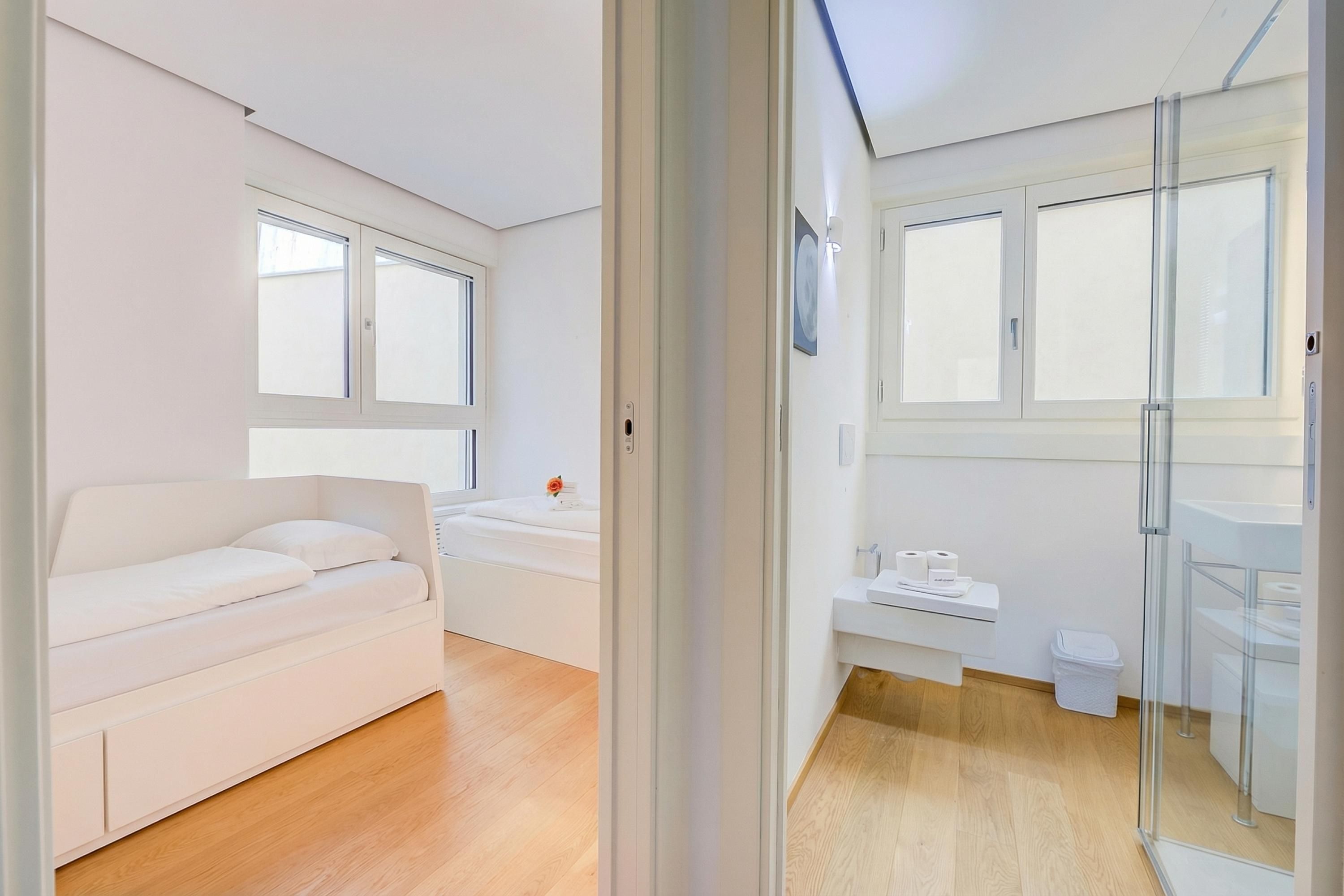 Una habitación moderna y bien iluminada con sofá, cabina de ducha de vidrio y baño pequeño con lavamanos e inodoro.