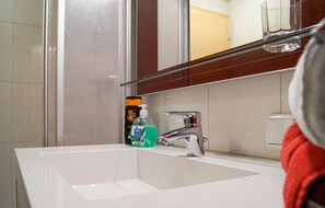 Een badkamer met een witte wastafel, een chromen kraan en een douchecabine van glas.