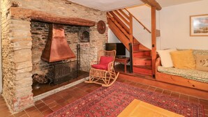 Un salón acogedor con chimenea de piedra, una escalera de madera, un sillón mecedor de mimbre y una alfombra estampada.