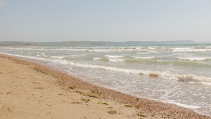 Una playa con olas, piedras y colinas a lo lejos.