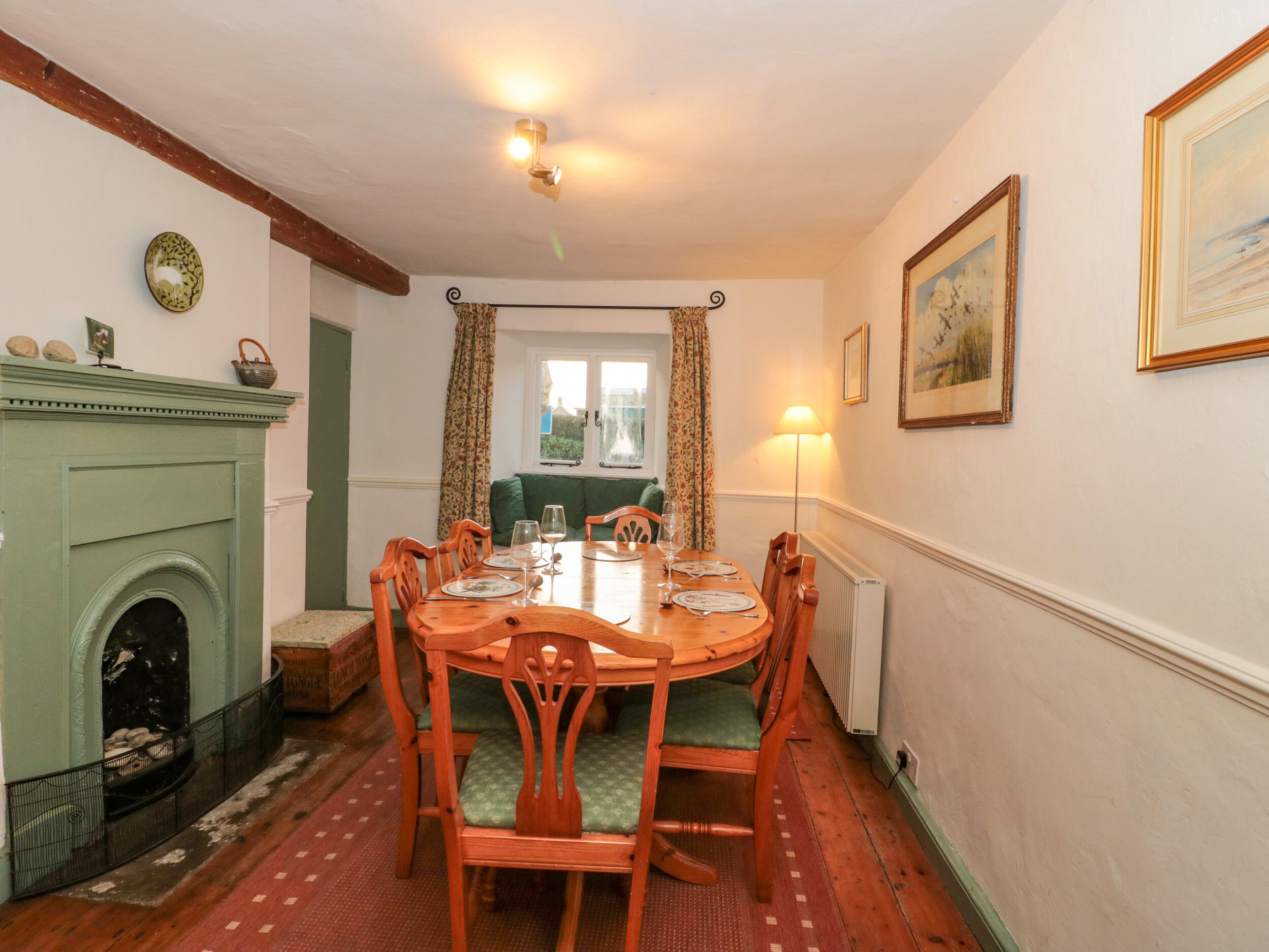 A dining room with a wooden table, chairs, a fireplace, and a window with curtains.