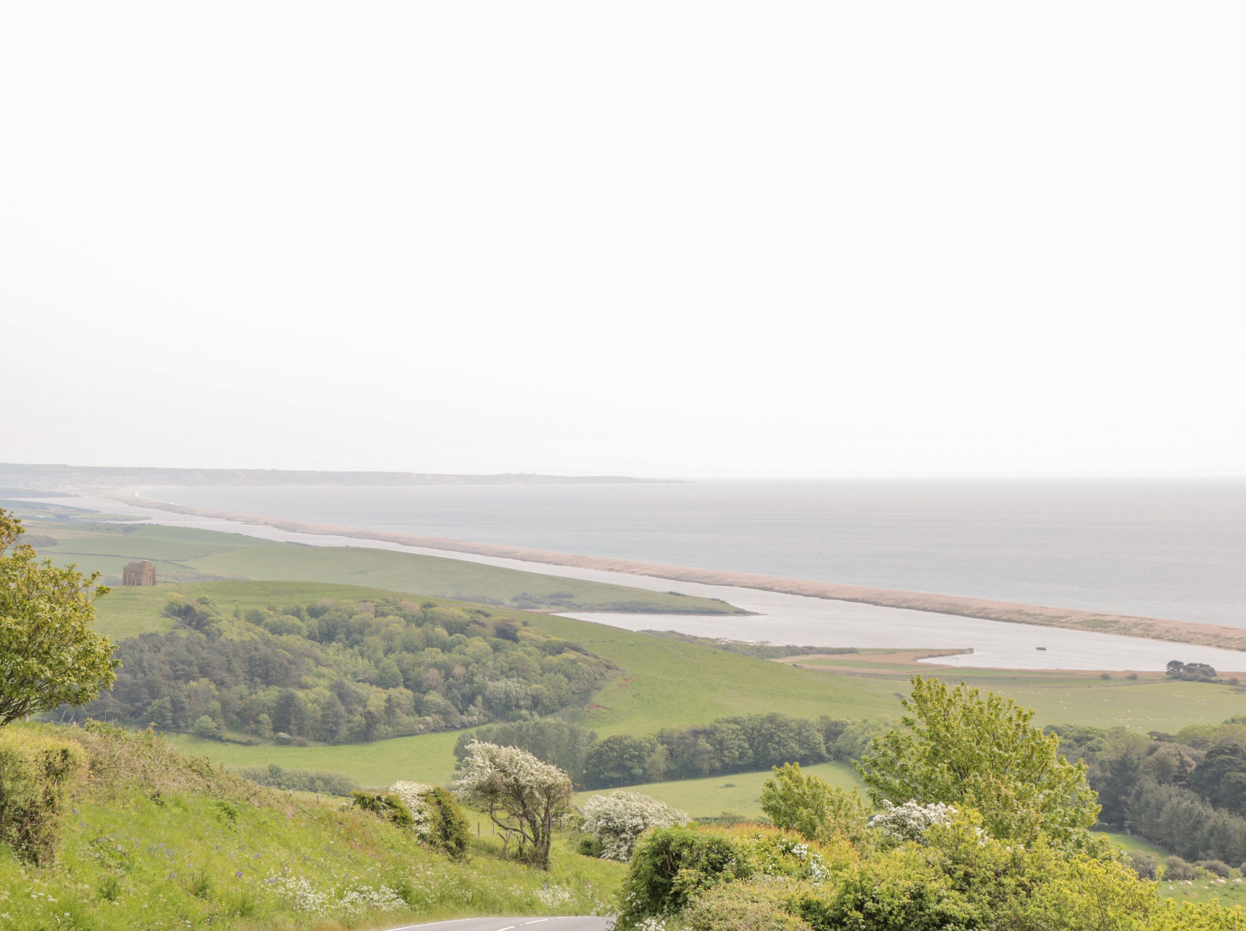 Et kystlandskab med en vej, grønne marker og en strand i det fjerne.