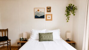 Un lit bien fait, avec du linge de lit blanc, un coussin à motifs verts et deux lampes de chevet.