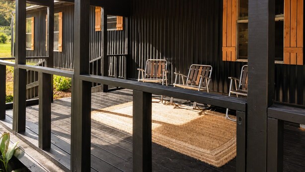 Une véranda avec des chaises en bois, un tapis tissé et une vue sur l’extérieur.