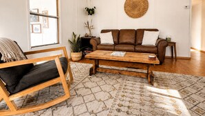 Un salon avec un canapé en cuir marron, une table basse en bois, un tapis à motifs et une grande fenêtre.