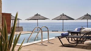 Zona junto a la piscina con sillones de descanso, sombrillas y vista al océano.