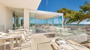 An outdoor dining area with glass walls, white furniture, and a view of the sea. - Hotel Perla Saracena - Suite La Perla (Salve)